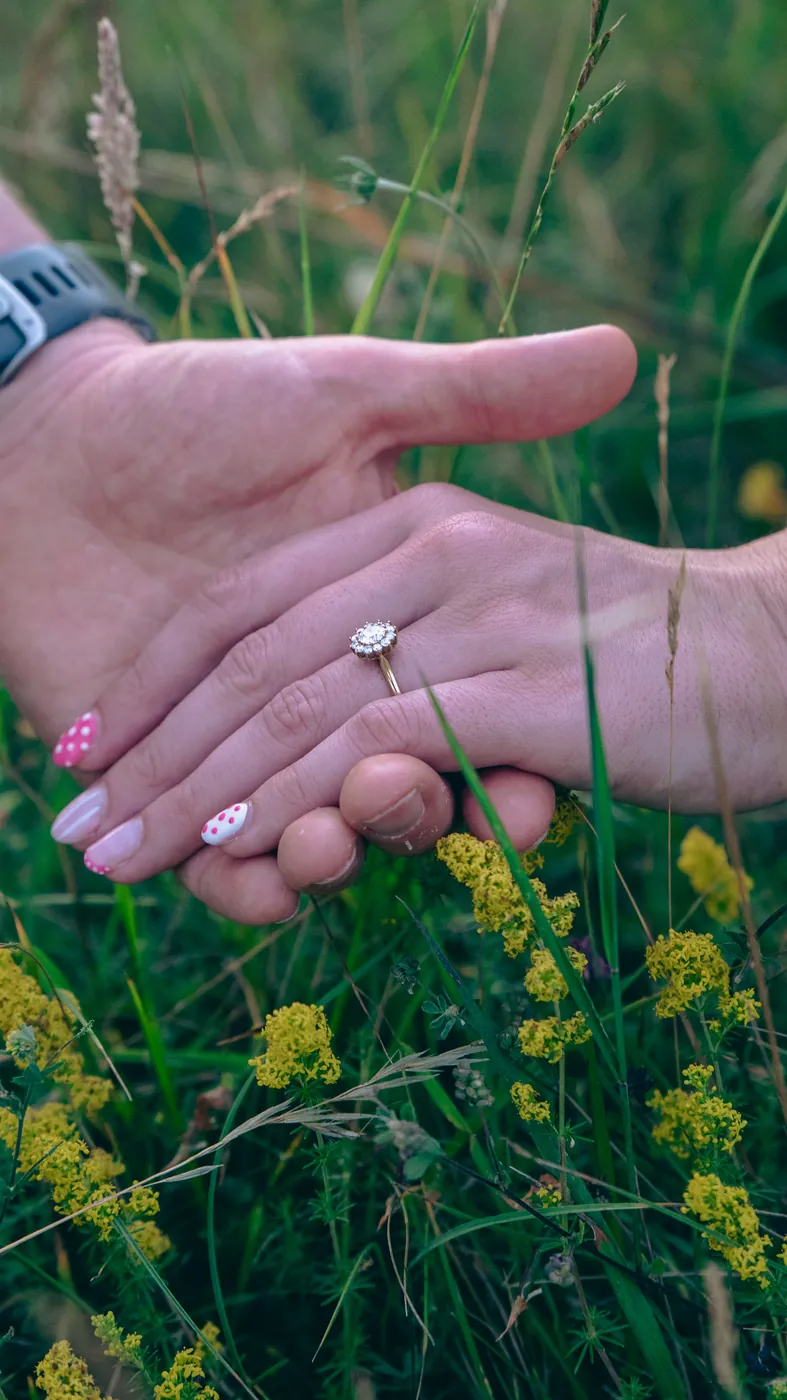 Surprise proposal photographer London engagement ring and held hands in a meadow